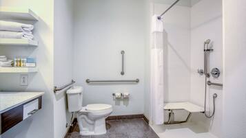 A modern bathroom with a toilet, handrails, a shower area, and a sink with a towel rack.