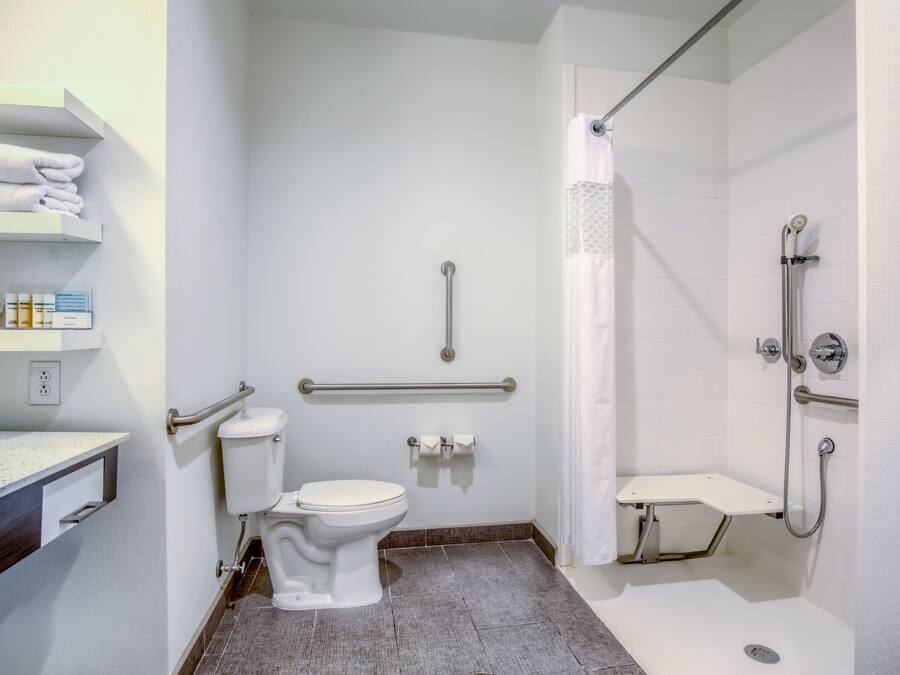 A modern bathroom with a toilet, handrails, a shower area, and a sink with a towel rack.