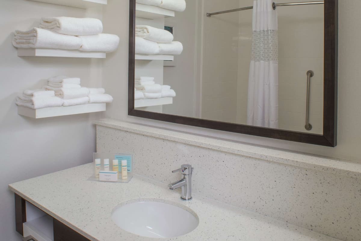 A modern bathroom with a large mirror, white towels on shelves, a sink, and toiletries.