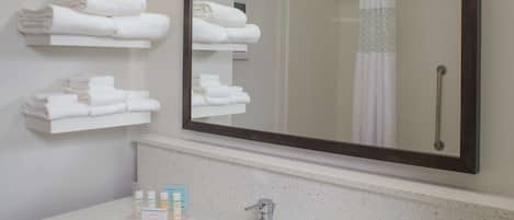 A modern bathroom with a large mirror, white towels on shelves, a sink, and toiletries.