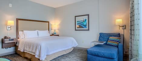 A hotel room with a bed, a chair, a nightstand, a lamp, a picture on the wall, and a window with curtains.