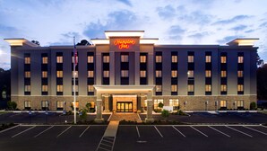 Un hotel Hampton Inn con una fachada moderna, una entrada bien iluminada y un estacionamiento.
