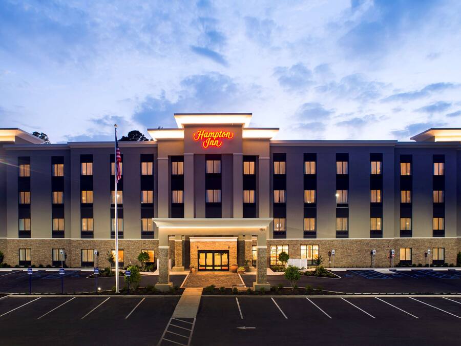Ein Hampton Inn Hotel mit moderner Fassade, einem gut beleuchteten Eingang und einem Parkplatz.