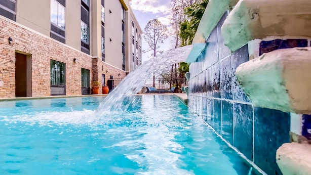 Una piscina con fuente de agua, rodeada por un edificio de ladrillo y un muro de azulejos.