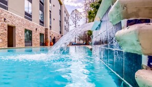 A swimming pool with a water feature, surrounded by a brick building and a tiled wall. - Hampton Inn Gulf Shores (Gulf Shores)