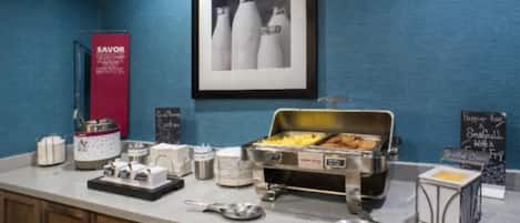 Un comptoir de petit-déjeuner avec divers aliments et condiments, un tableau encadré au mur et une enseigne indiquant « SAVOR ».