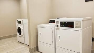 A laundry room with three white front-loading washers and dryers, a beige wall, and a sign stating Hampton Inn is not responsible for lost, stolen, or damaged items.