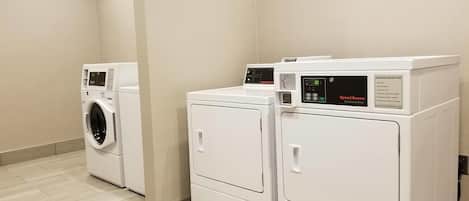 A laundry room with three white front-loading washers and dryers, a beige wall, and a sign stating Hampton Inn is not responsible for lost, stolen, or damaged items.