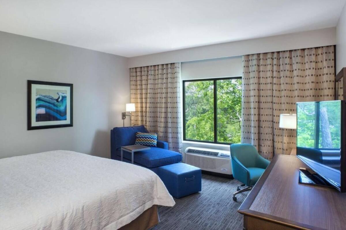 A hotel room with a bed, a desk, a chair, a TV, and a window with curtains.