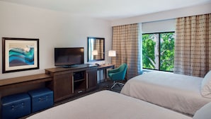 Habitación de hotel con dos camas, un escritorio con televisor, una silla y un ventanal con cortinas.