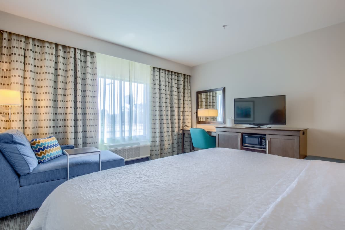 A hotel room with a large bed, a desk with a television, a microwave, and a chair.