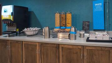 Una estación de café de servicio propio con una máquina de café, dispensadores y un letrero que dice 'TASTE POUR MIX LAYER LAUGH'.