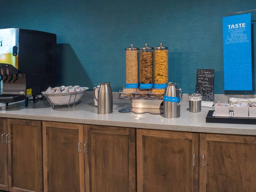 A self-serve coffee station with a coffee machine, dispensers, and a sign that reads "TASTE POUR MIX LAYER LAUGH."