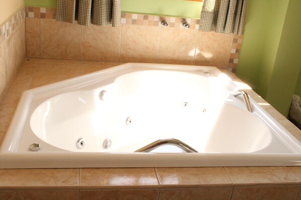 A large, rectangular, white bathtub with a single faucet, set in a bathroom with beige tiles and a green wall. - Pousada Alemã (Santo Antonio do Pinhal)
