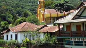 A rural village with a church featuring a bell tower, surrounded by houses with tiled roofs. - Pousada Alemã (Santo Antonio do Pinhal)