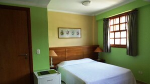 A bedroom with a bed, a small refrigerator, a window with curtains, and a wall-mounted picture. - Pousada Alemã (Santo Antonio do Pinhal)