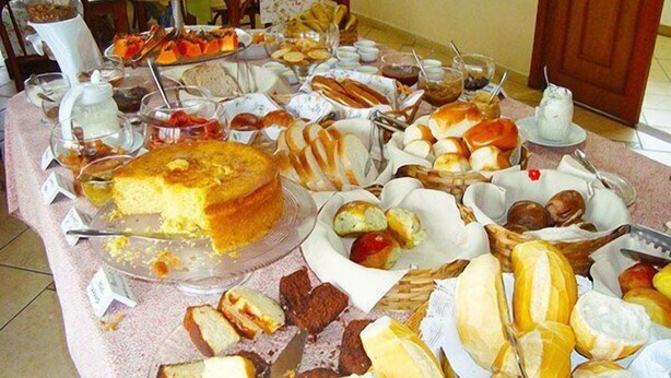 A buffet table with various food items including cakes, pastries, and bread. - Pousada Alemã (Santo Antonio do Pinhal)
