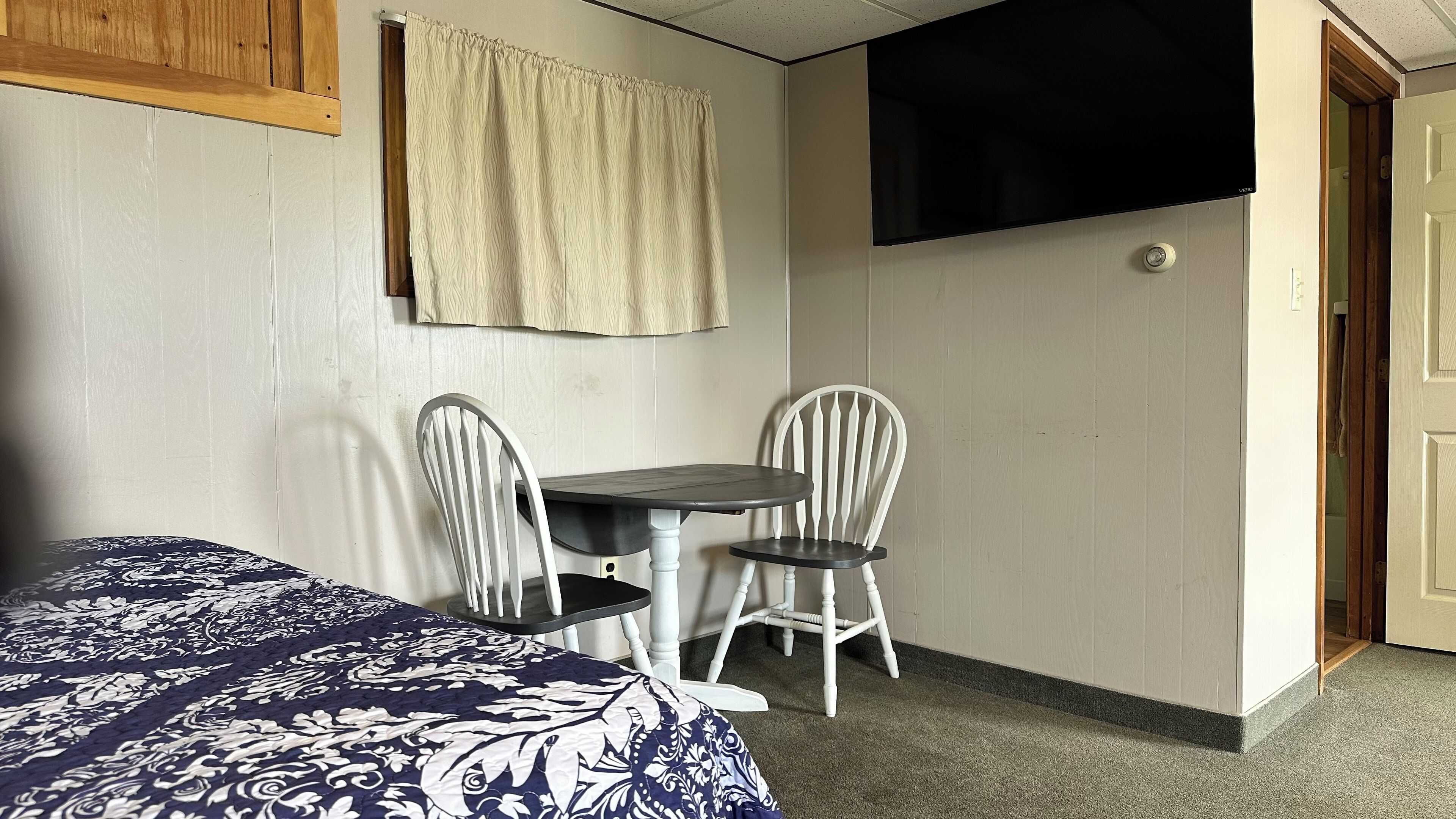 A room with a bed, a small table with two chairs, a television, and a door.