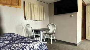 A room with a bed, a small table with two chairs, a television, and a door.
