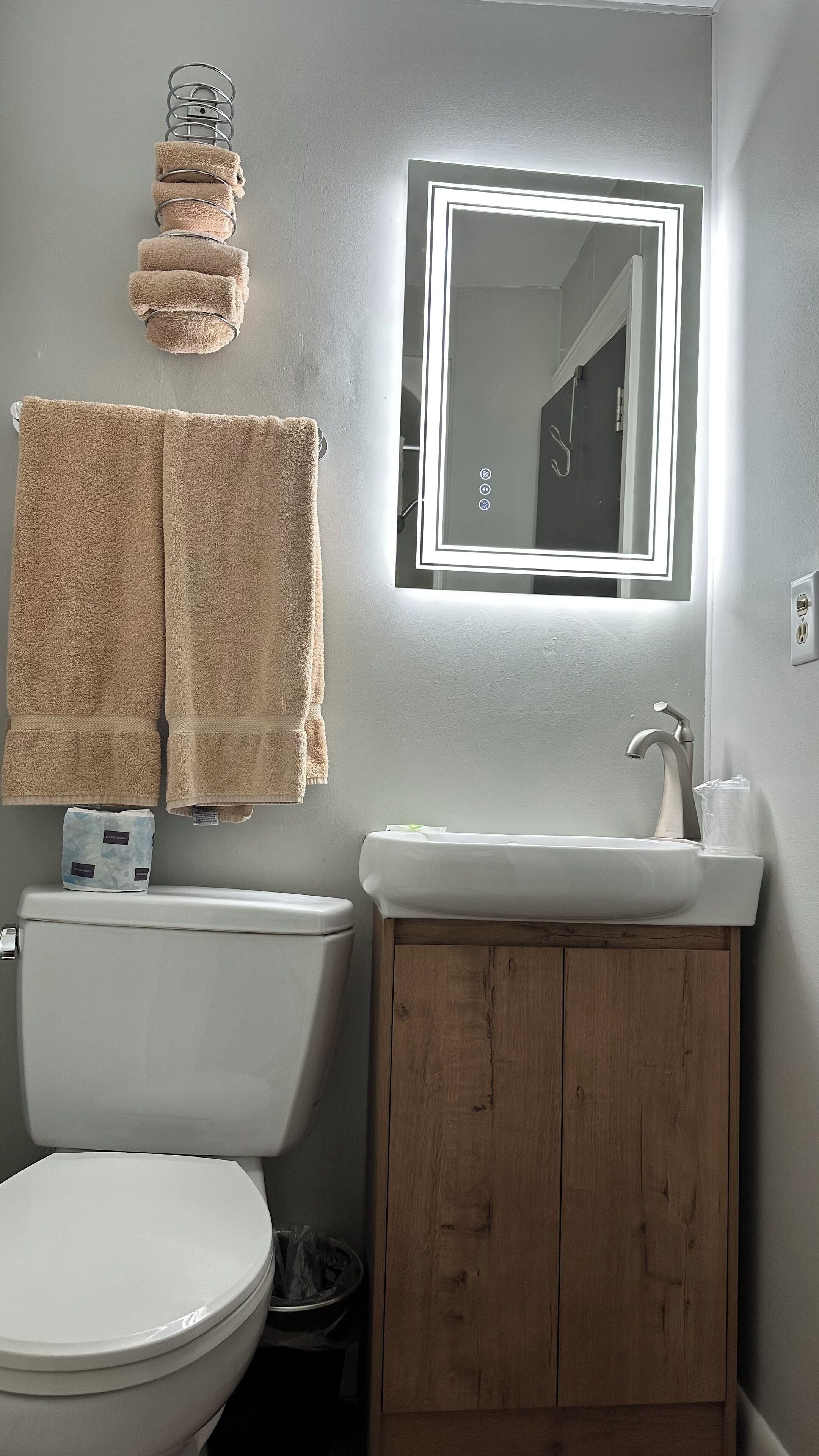 A bathroom with a toilet, sink, wooden cabinet, and a towel rack with multiple towels.