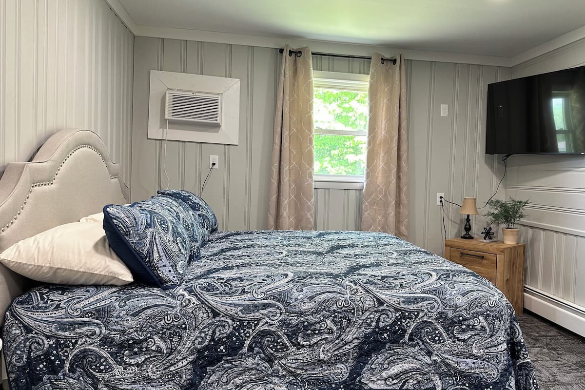 A bedroom with a bed, a nightstand, a TV, and a window with curtains.