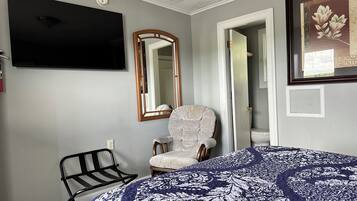 A bedroom with a bed, a chair, a television, a mirror, and a door leading to a bathroom.