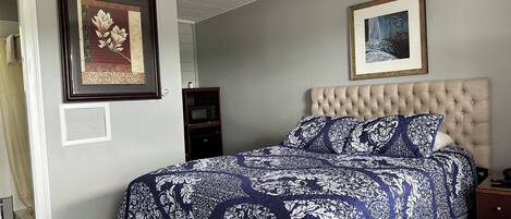 Un dormitorio con una cabecera capitonada, una colcha estampada y dos cuadros en la pared.