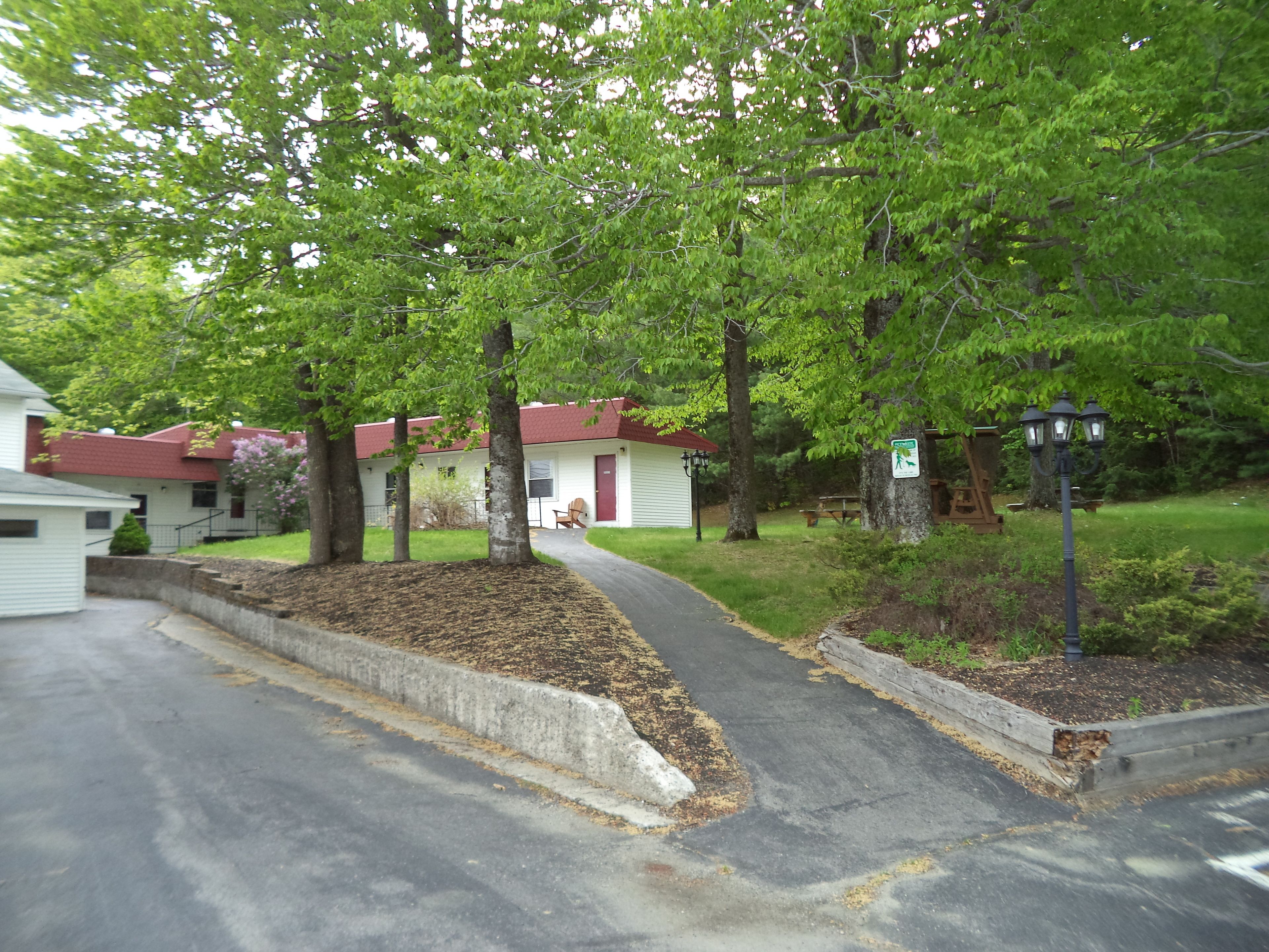 A row of white cabins with red roofs, surrounded by trees and a paved path.