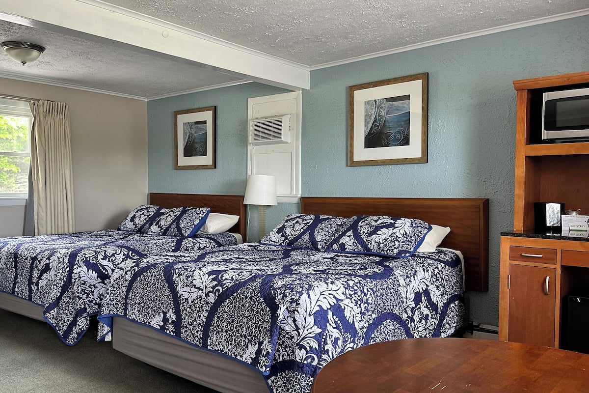 A hotel room with two beds, a wooden cabinet, a television, and framed pictures on the wall.