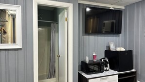 Ein Badezimmer mit Dusche, Spiegel, Waschbecken und einem Kaffeeautomaten sowie einem schwarzen Kühlschrank.