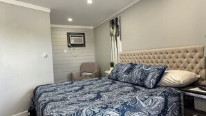 Ein Schlafzimmer mit einer karriert vorgetieften Kopfteil, einer gemusterten Tagesdecke, einem Sessel und einer Wand-Klimaanlage.
