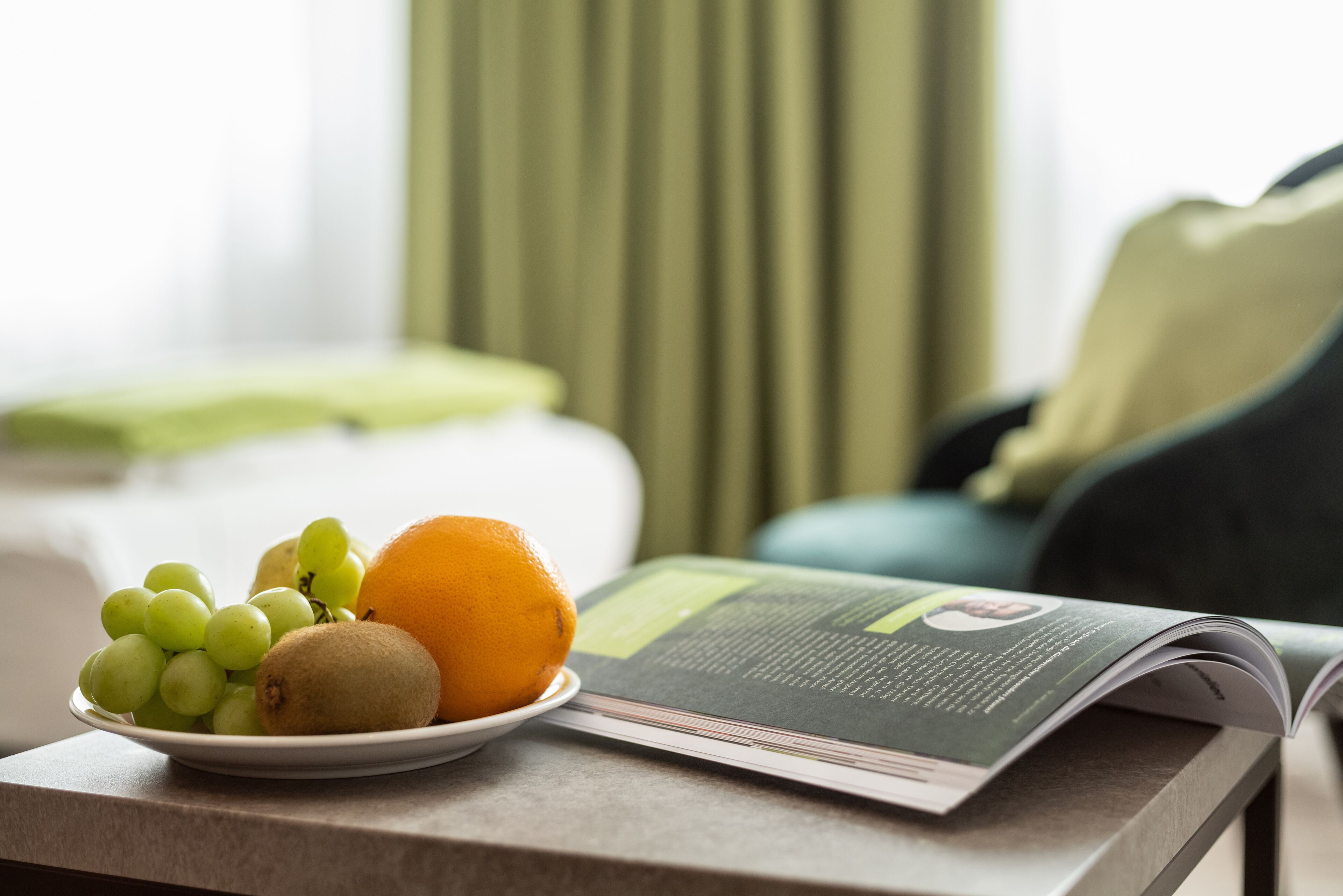 A plate with grapes, an orange, and a kiwi on a table with a magazine.