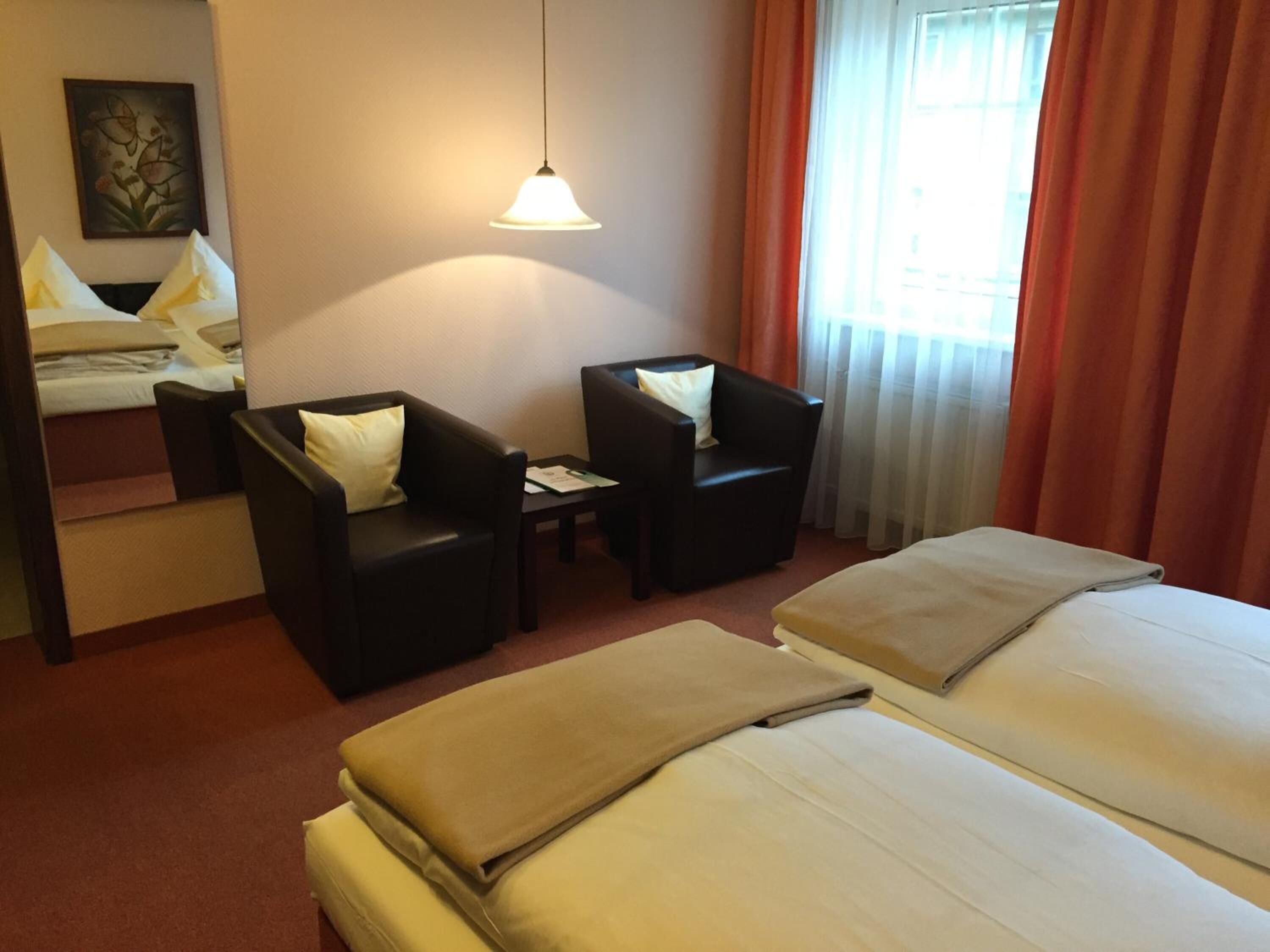 Ein Hotelzimmer mit einem Bett, zwei Sesseln, einem kleinen Tisch und einer Hängelampe.