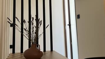 Een kamer met een houten tafel, een vaas met gedroogde bloemen, een zwart-wit gestreept scheidingswand, een wandgemonteerde flatscreen-tv en een raam met gordijnen.