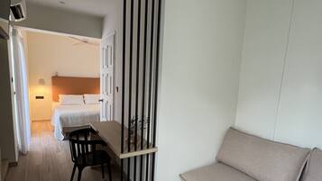 Una habitación moderna y minimalista con suelo de madera, un sofá beige, una mesa de comedor con sillas y un separador negro.