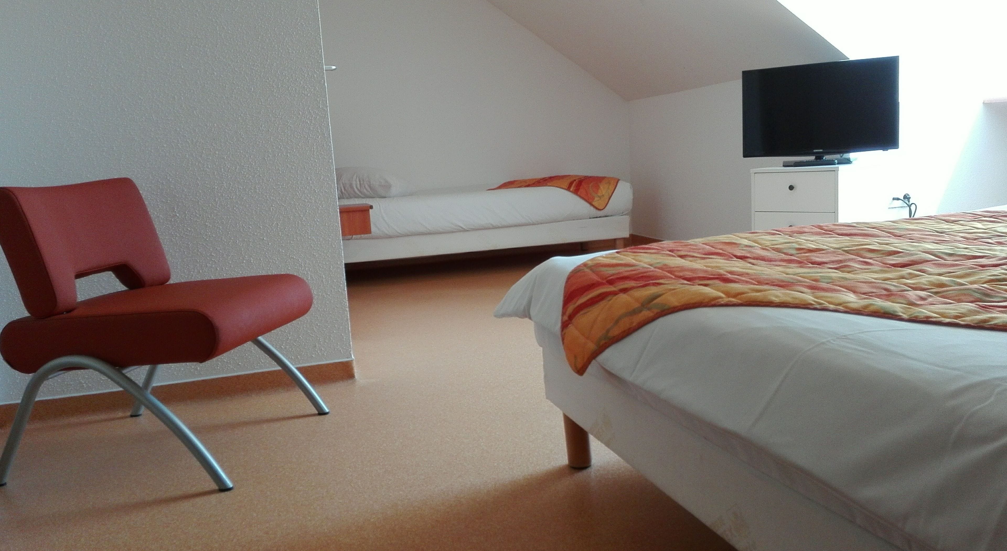 A bedroom with a bed, a red chair, a television, and a white wardrobe.