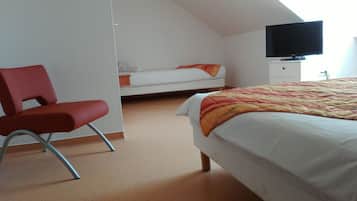 A bedroom with a bed, a red chair, a television, and a white wardrobe.