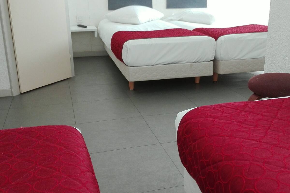 A hotel room with a bed, a nightstand, and a red quilted bedspread.