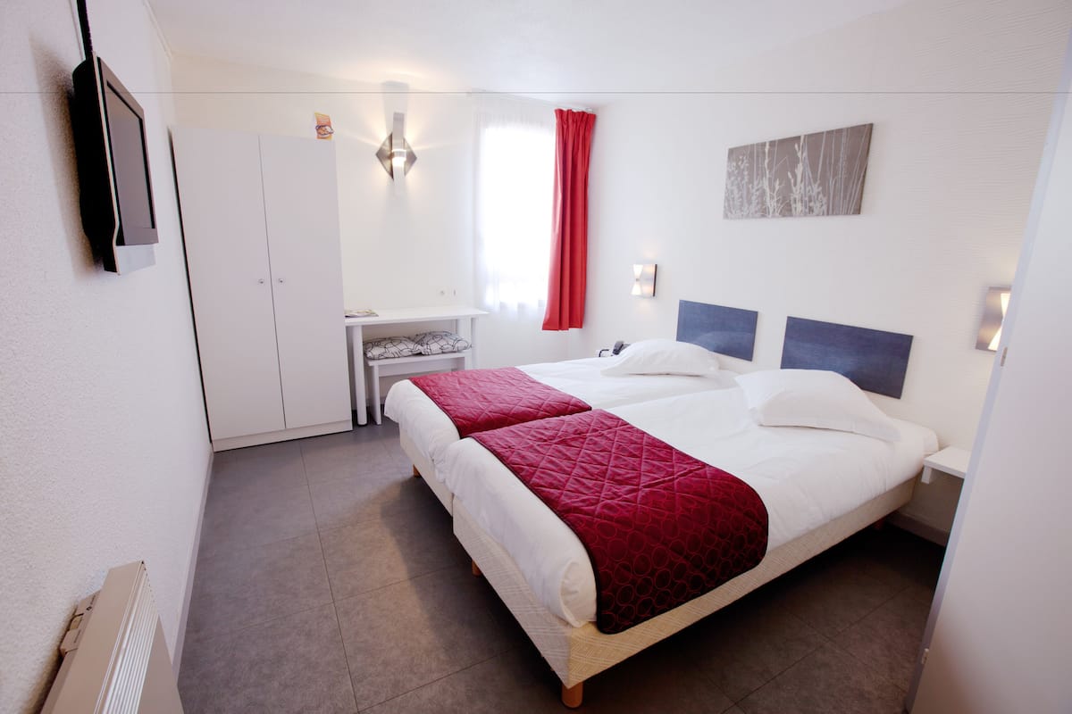 A double bed with a red quilt, a bedside table, a mirror, and a wall-mounted TV.