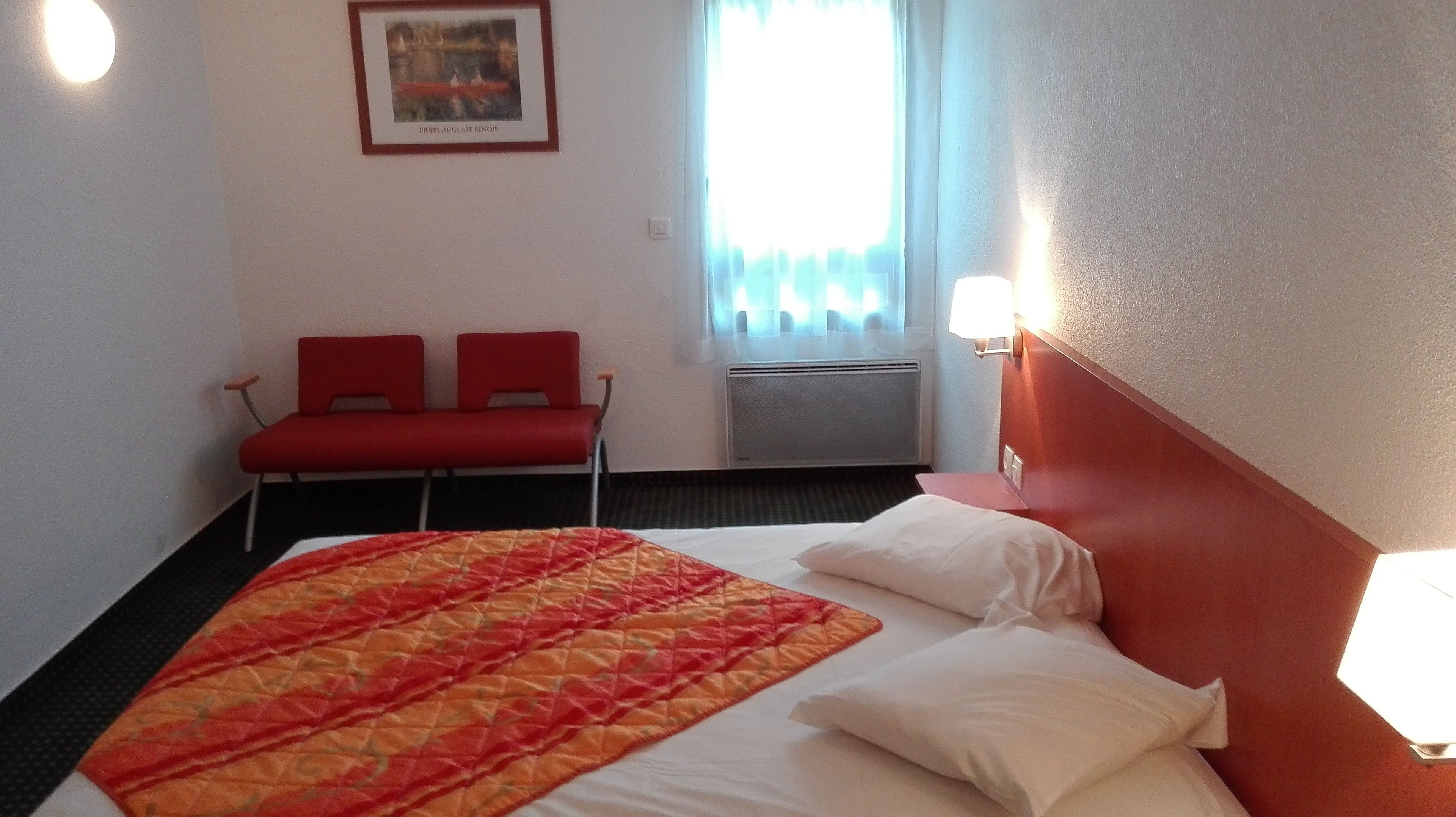 Une chambre d’hôtel avec un lit, une chaise rouge, une fenêtre avec des rideaux et un tableau encadré au mur.