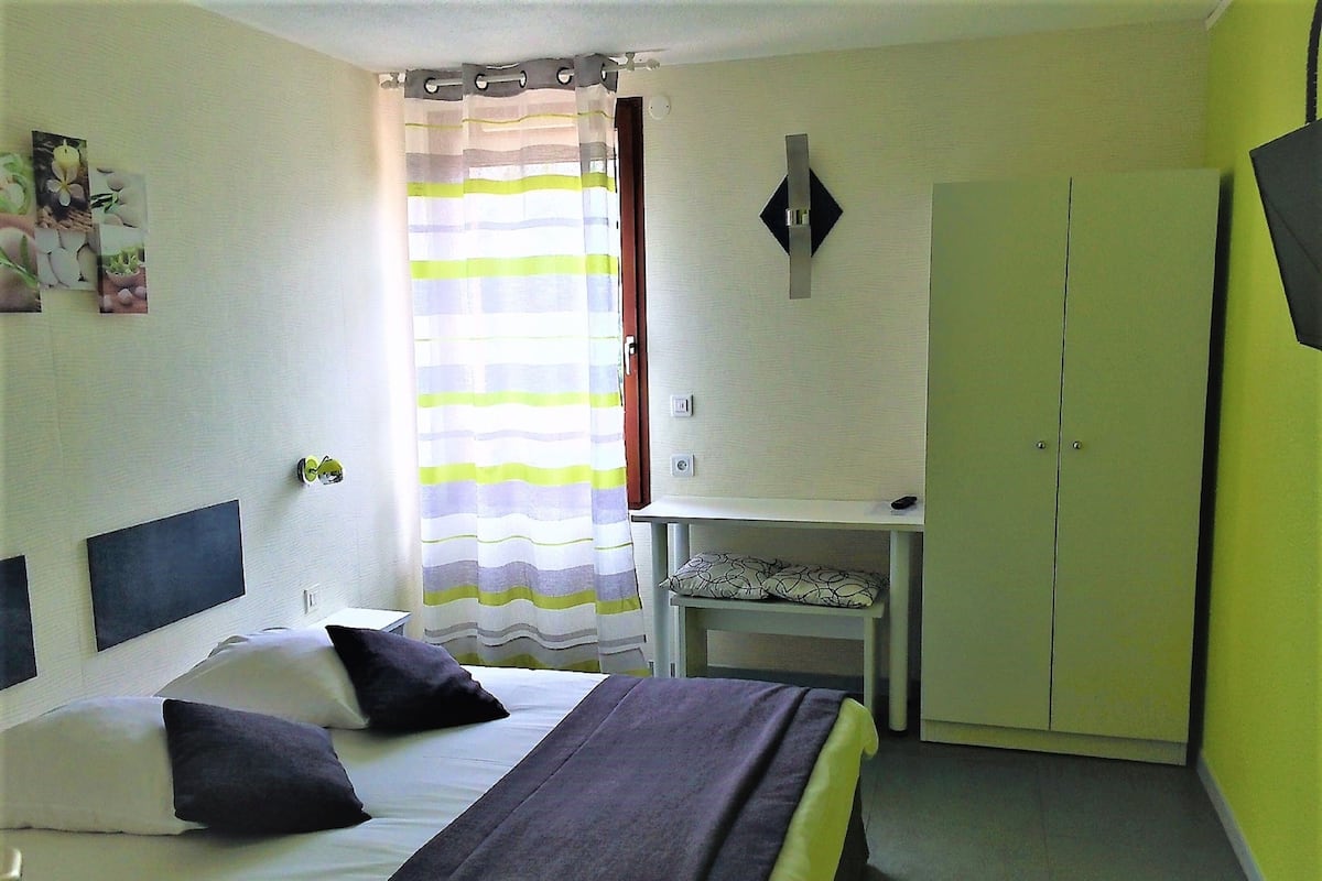 A bedroom with a bed, pillows, a bedside table, a wardrobe, and a curtain.