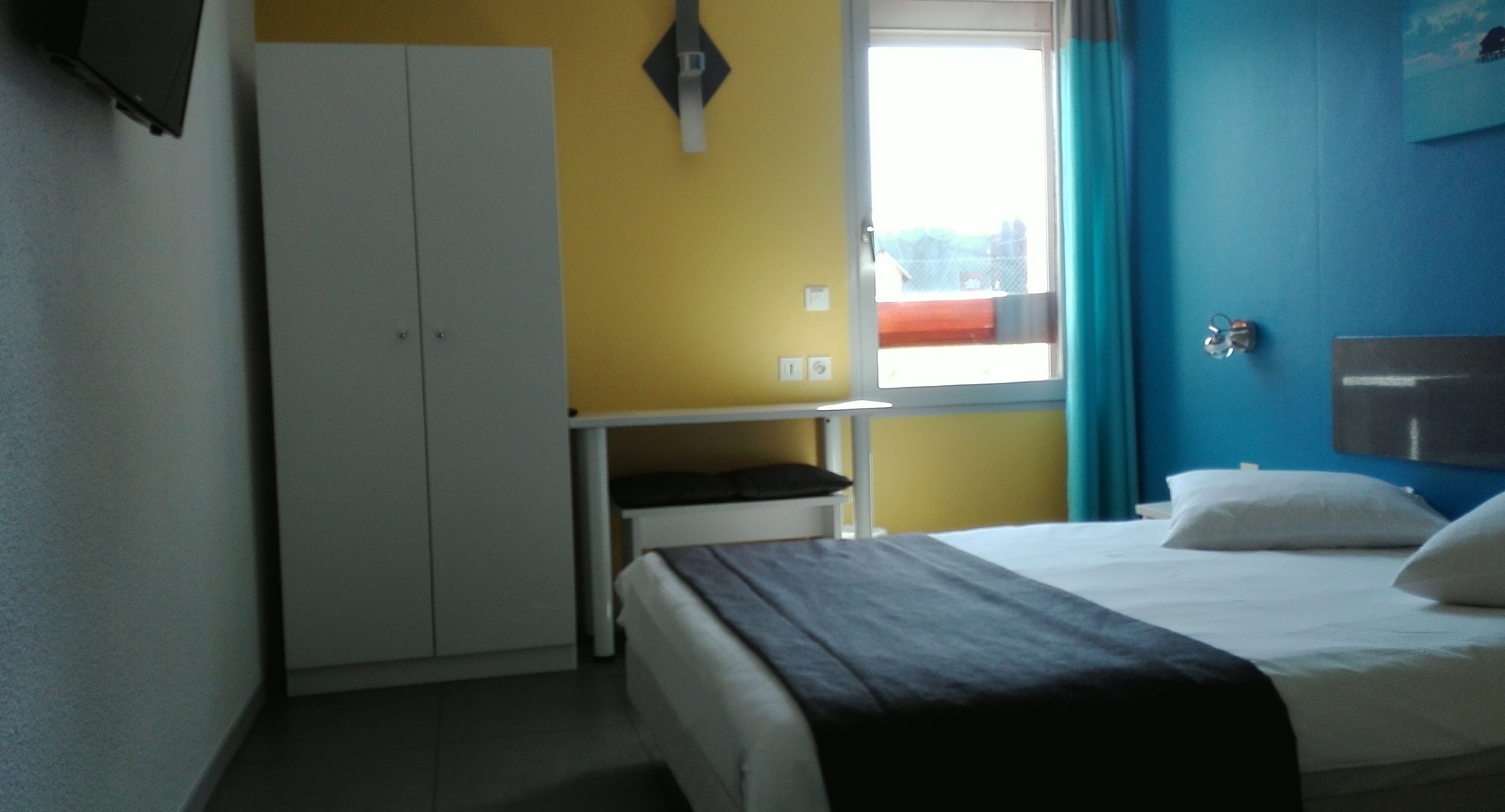 Ein Schlafzimmer mit Bett, Kleiderschrank, Schreibtisch und einem Fenster mit Vorhängen.