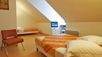 A modern bedroom with a sloped ceiling, a bed with a colorful blanket, a chair, a desk with a computer, and a window providing natural light.