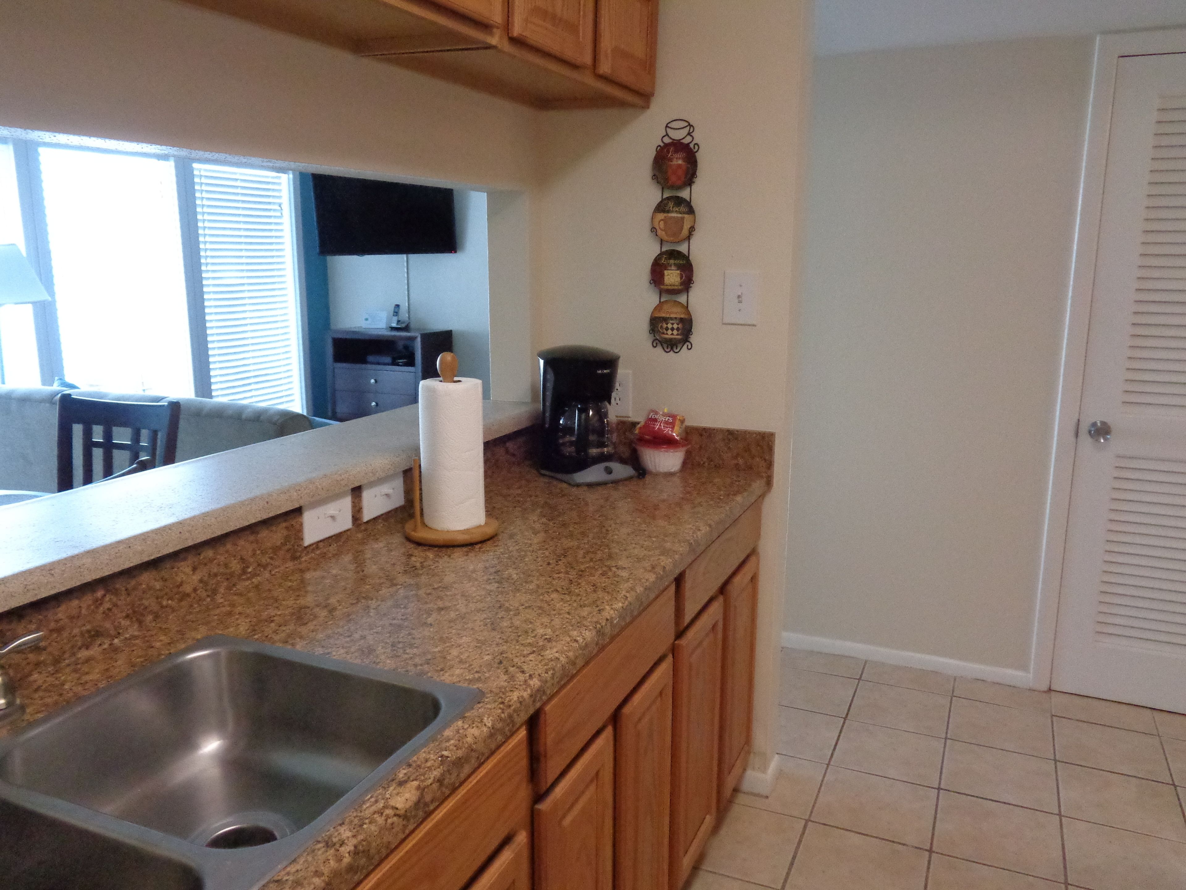 A kitchen with a granite countertop, wooden cabinets, a stainless steel sink, a coffee maker, and a wall-mounted decorative item.