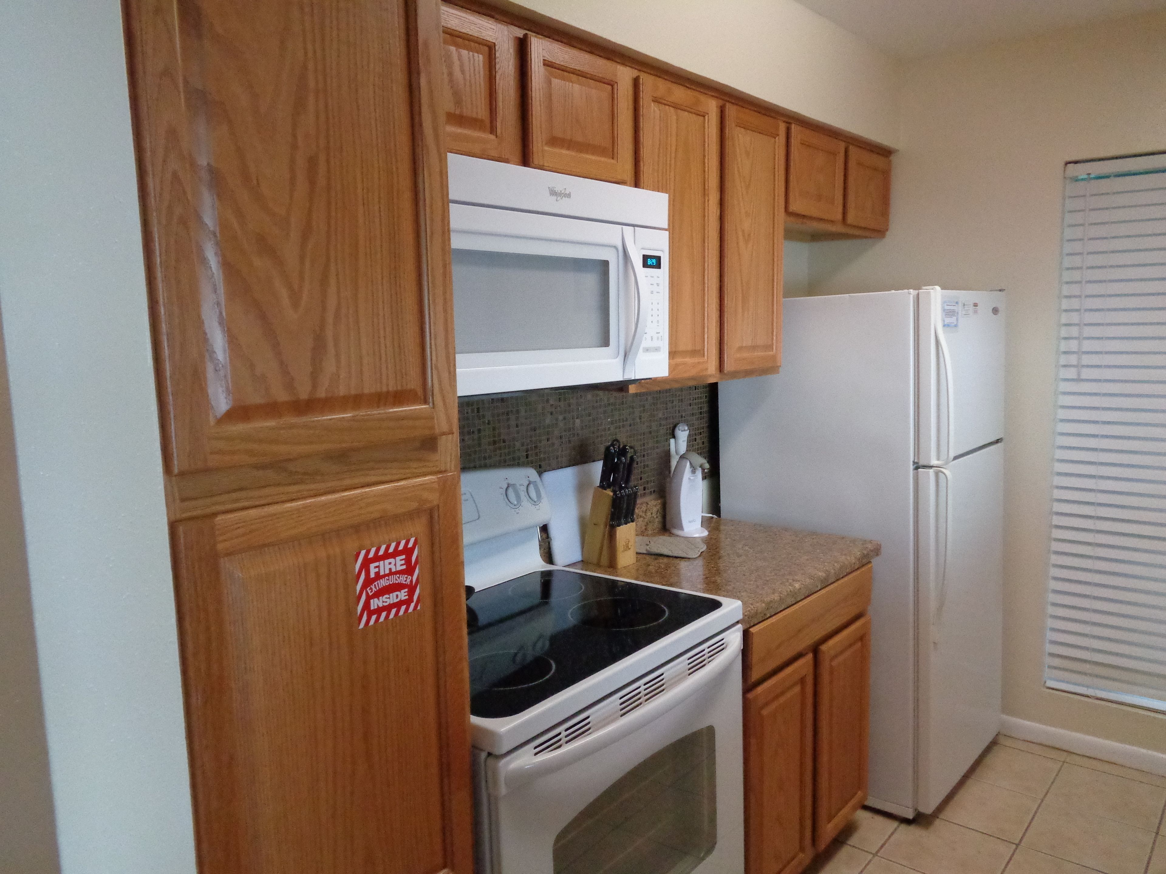 A kitchen with wooden cabinets, a white microwave, a stove, and a refrigerator.