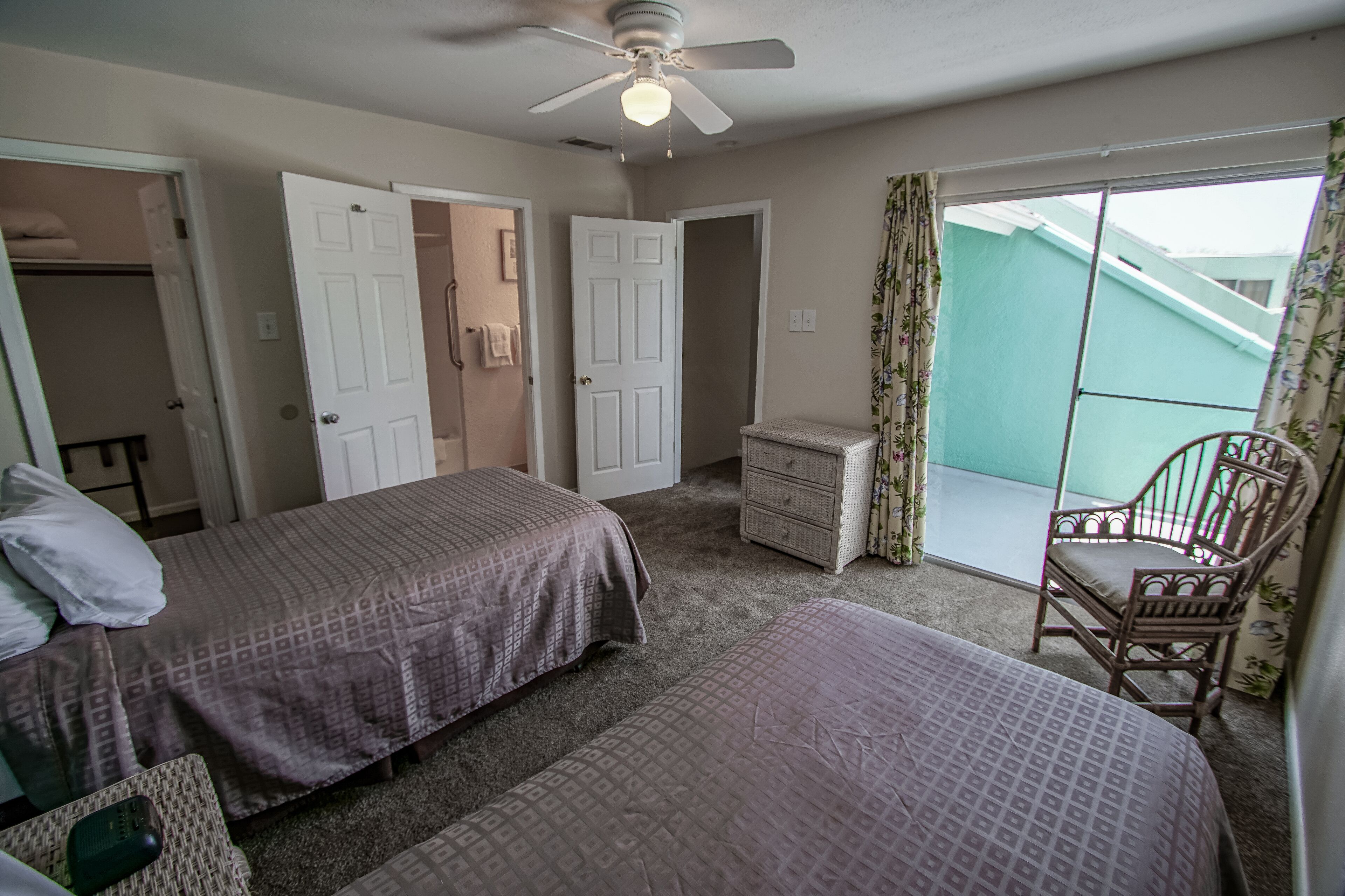 A bedroom with two beds, a dresser, a chair, and a balcony with a view.