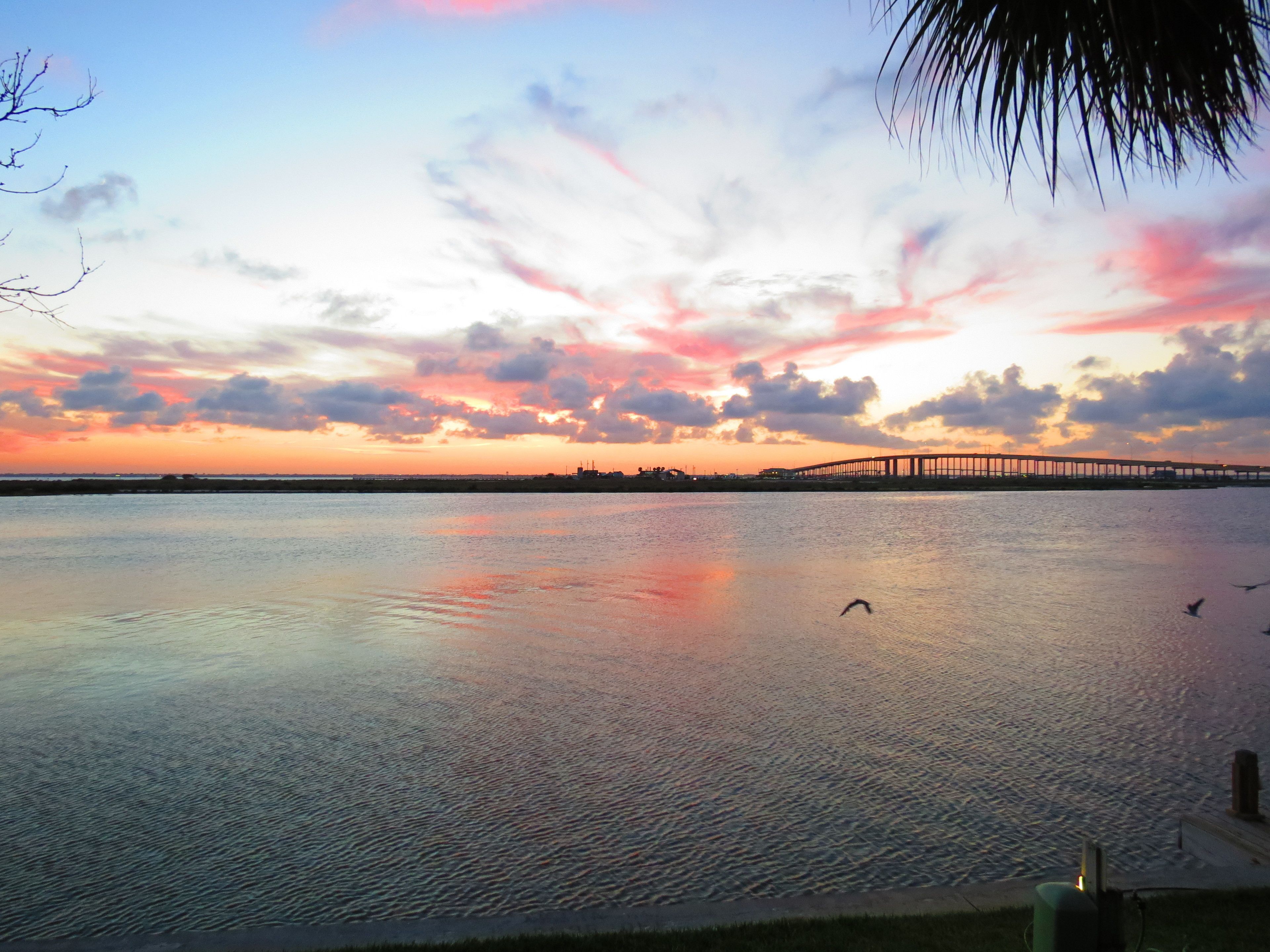 A sunset over a calm body of water with a bridge in the distance.