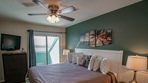 Une chambre à coucher comprenant un lit, un ventilateur de plafond, une télévision, une commode, une lampe et une vue sur l’extérieur.