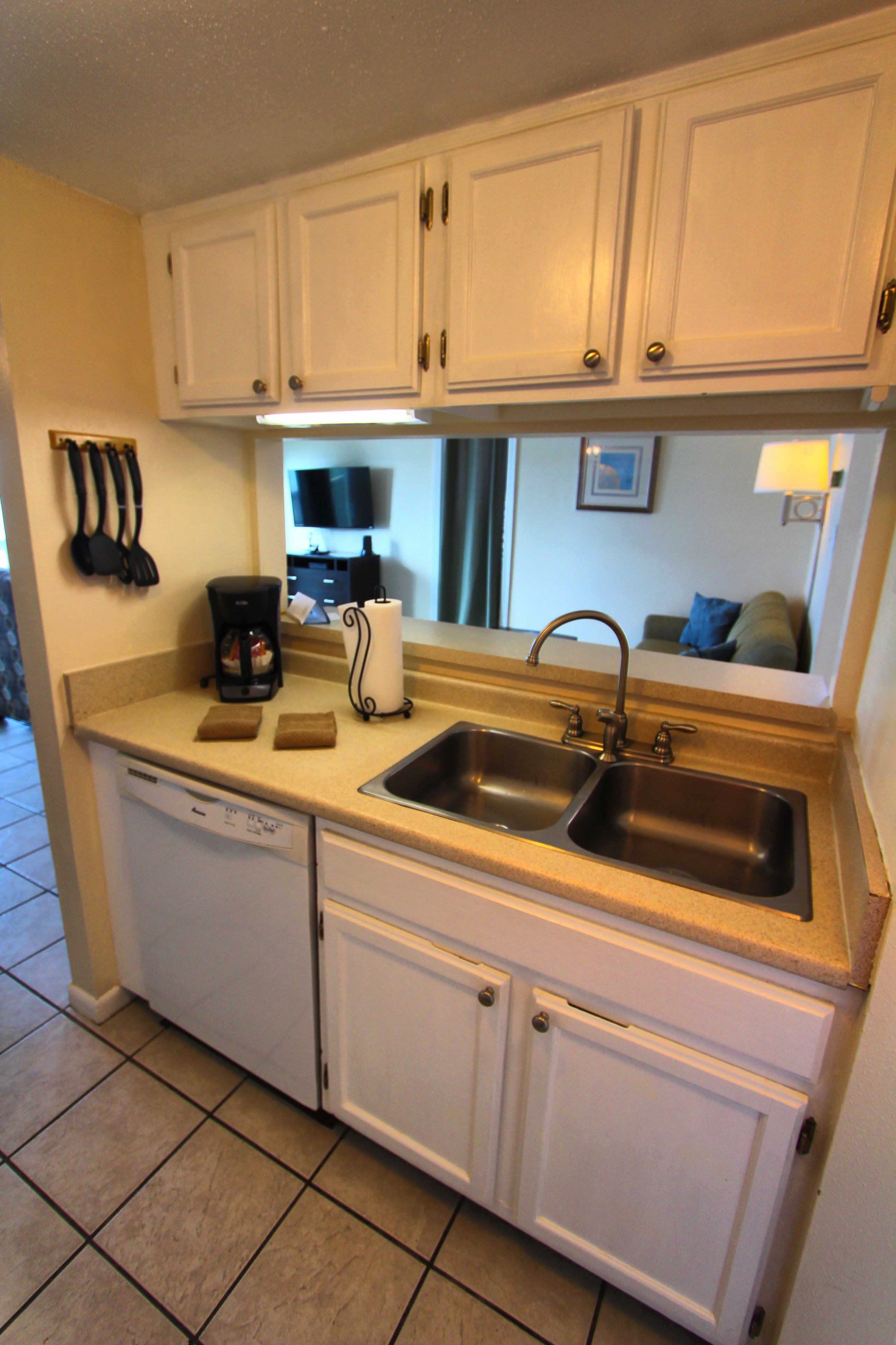 A compact kitchen with white cabinets, a dishwasher, a double sink, and a coffee maker.