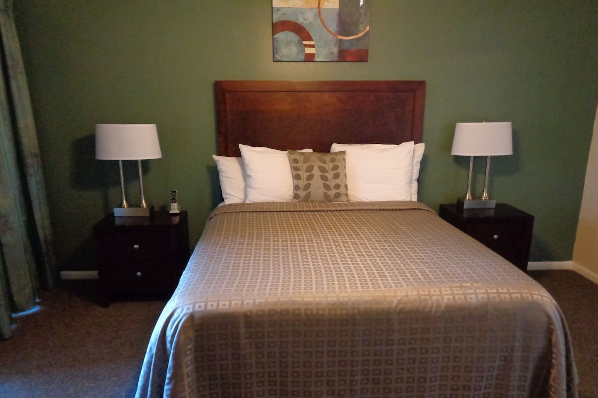 A neatly made bed with a patterned bedspread, two bedside tables with lamps, and a wall art piece above the bed.